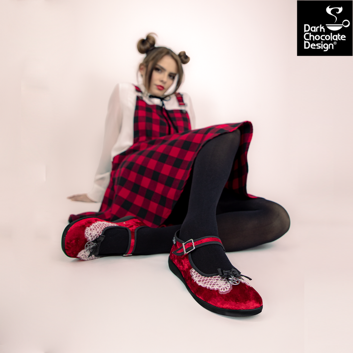 Person wearing a red and black checkered dress with matching shoes, sitting on a white background.