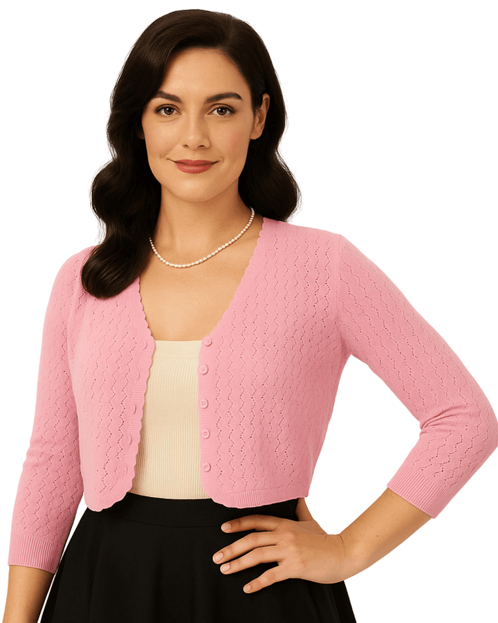 Vintage-inspired pink knit bolero with 3/4 sleeves, styled over a beige top and black skirt.
