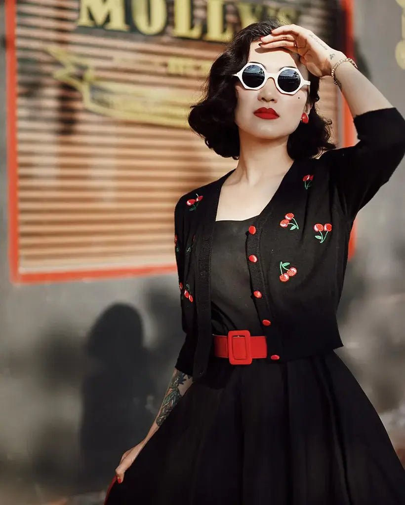Woman wearing a cropped cherry cardigan with V-neckline and playful embroidery, styled for a retro look.