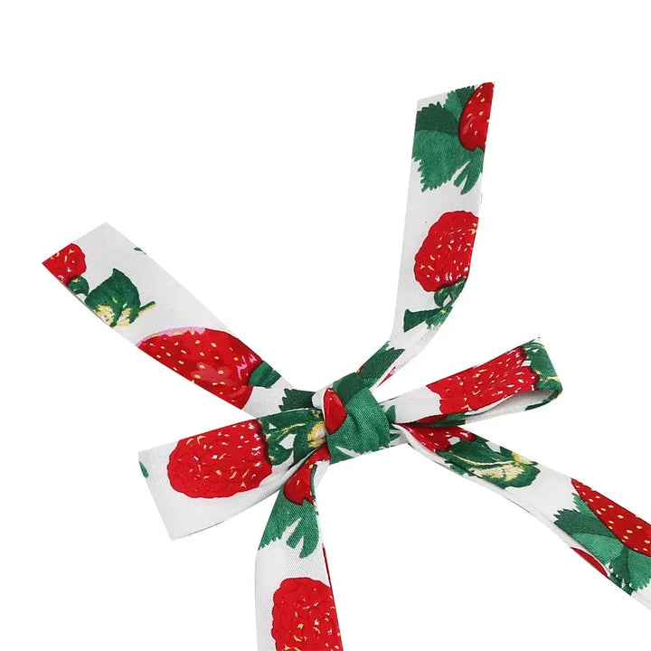 Close-up of a white ribbon bow with a vibrant strawberry print, perfect for accessorizing dresses.