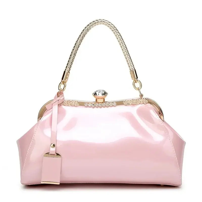 Stylish pink patent women's handbag with rhinestone clip lock and chain handle for modern elegance.