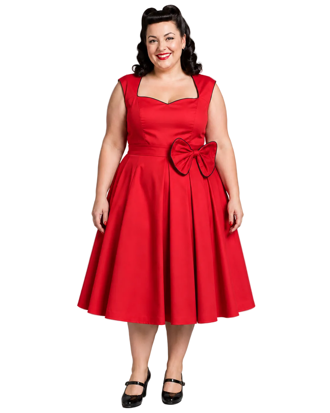 A woman modeling a bright red 1950s-style swing dress with a sweetheart neckline, square neckline trim, a large waist bow, and black Mary Jane shoes against a solid gray studio background.