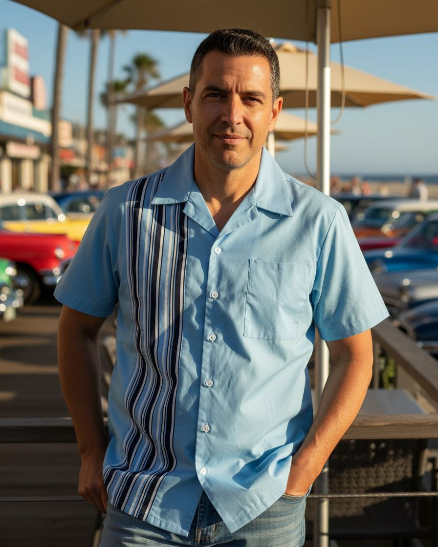 Man wearing a light blue shirt with a striped panel in an outdoor setting with cars and palm trees.