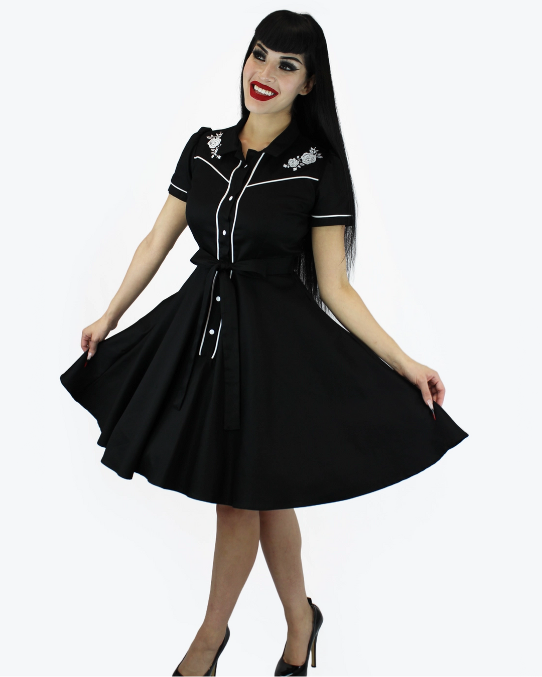 A woman modeling a black short-sleeve retro-style swing dress with white piping and silver floral embroidery on the chest, posed against a solid white background.