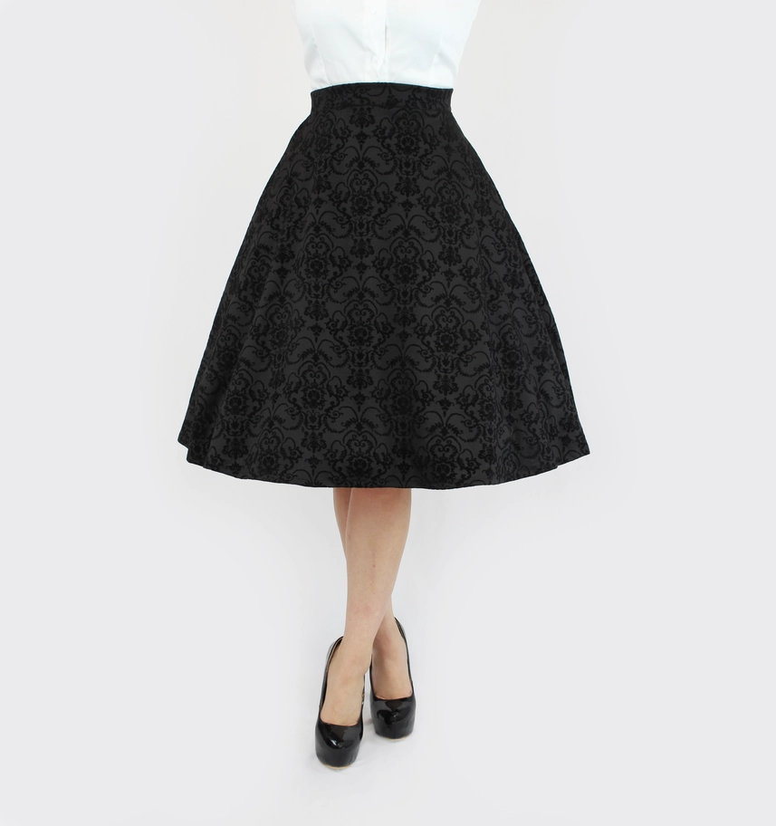 A black high-waisted A-line skirt with a textured damask brocade pattern, shown on a model wearing a white top and black heels against a plain white background.