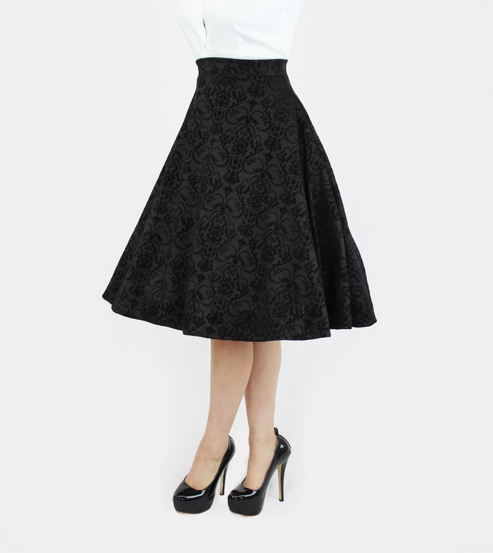 A black flared skirt with an intricate floral jacquard pattern, shown on a model wearing a white top and black high heels against a light gray background.