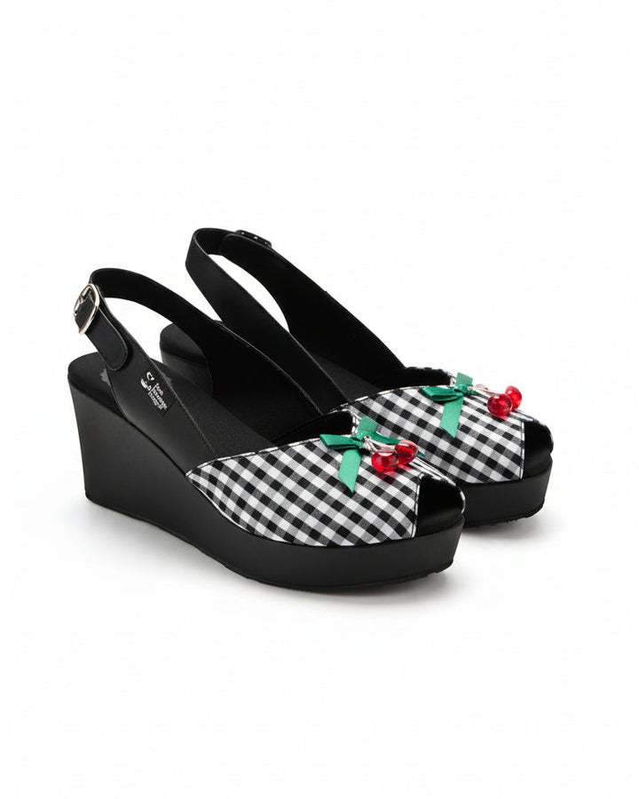 A pair of black wedge slingback sandals with a black and white gingham pattern on the toe area, decorated with green bows and red cherries, shown on a white background with a Dark Chocolate Design logo in the top right corner.