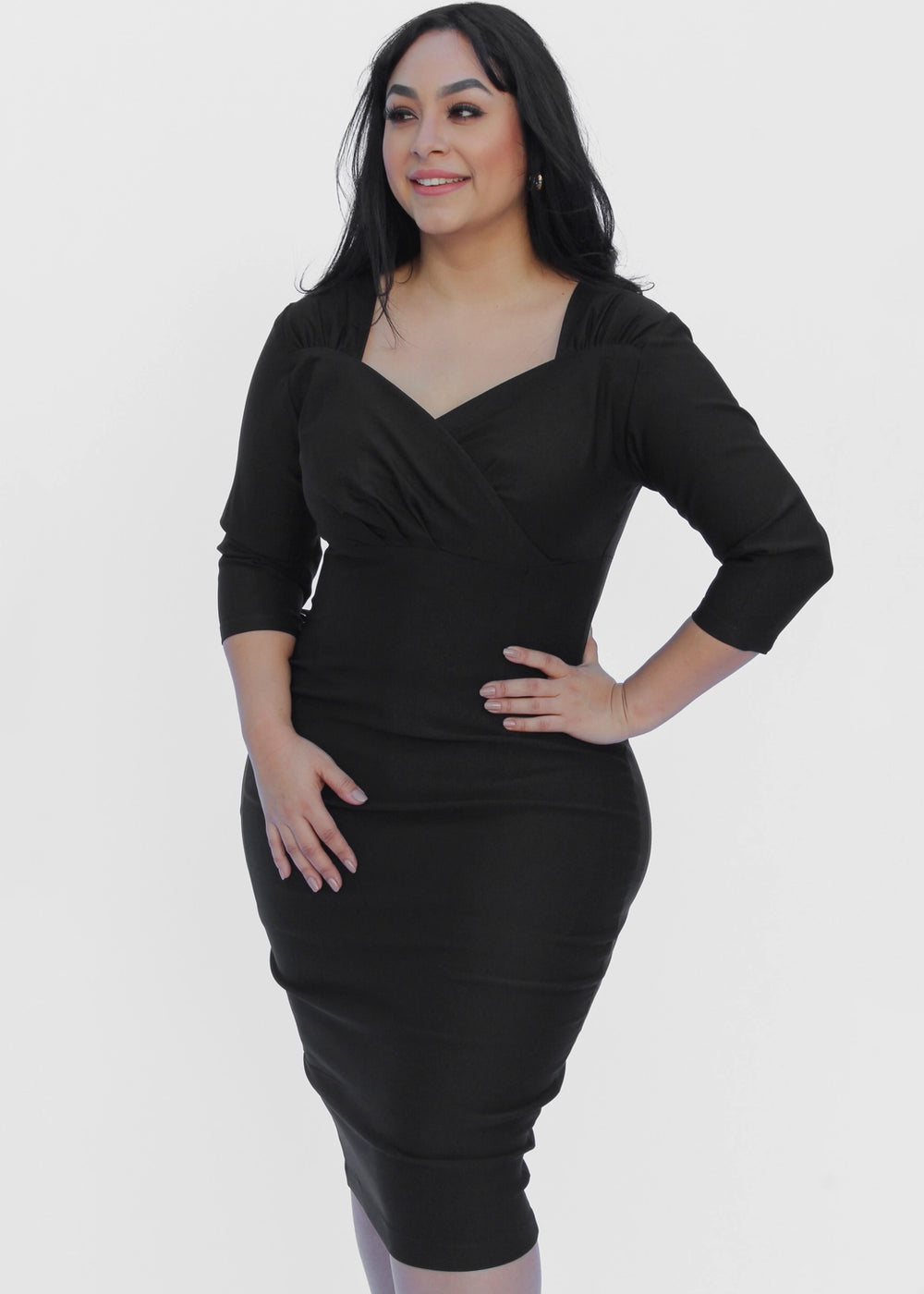 A woman modeling a black knee-length wrap-style dress with three-quarter sleeves against a plain light gray studio background.