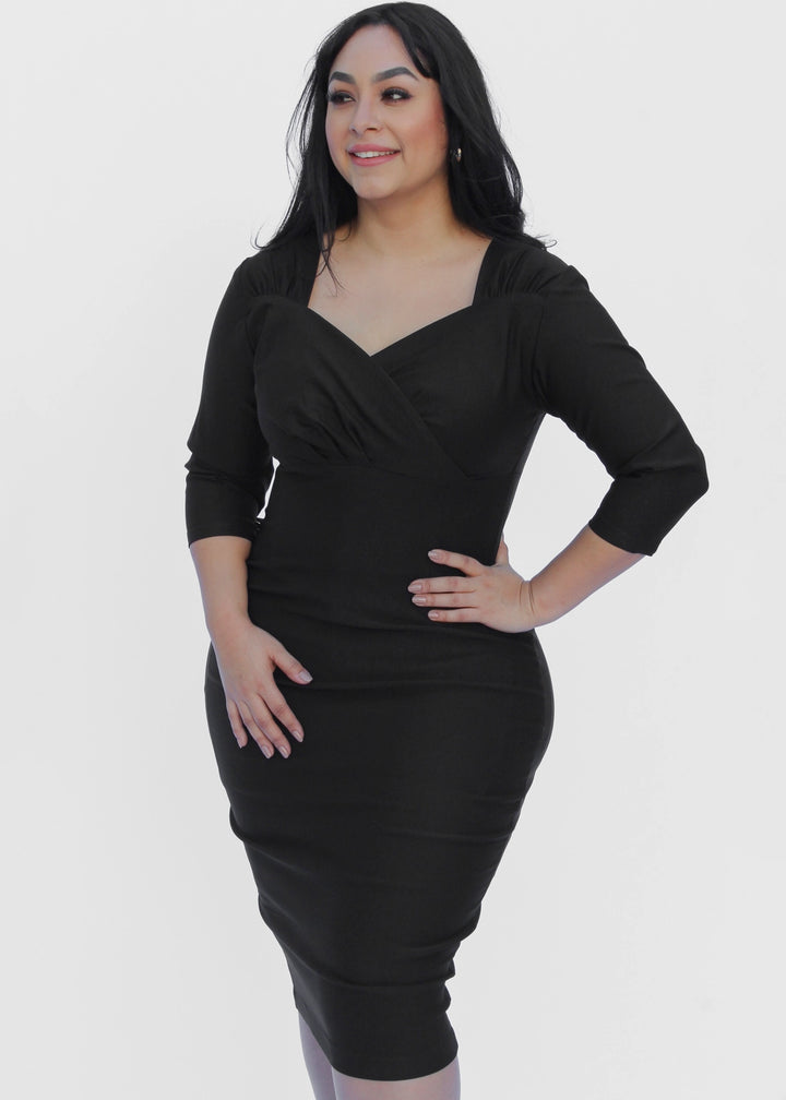 A woman modeling a black knee-length wrap-style dress with three-quarter sleeves against a plain light gray studio background.