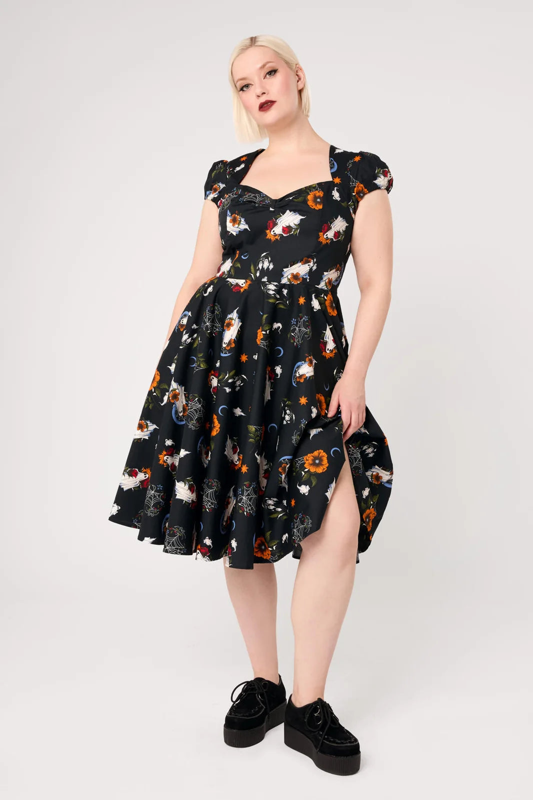 Plus size model wearing Hell Bunny Ghost Flower black 50s dress with full circle skirt and pockets