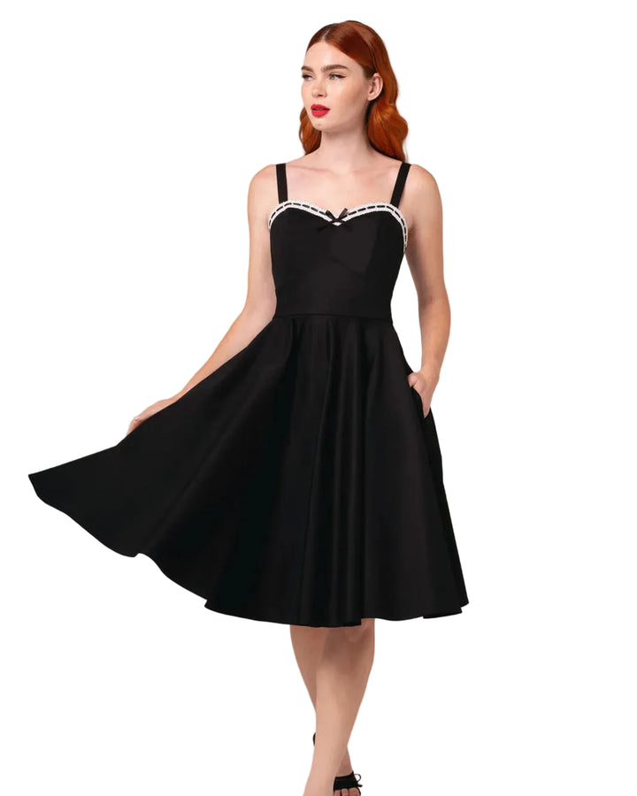 Woman wearing a black dress with a white lace trim on a plain background