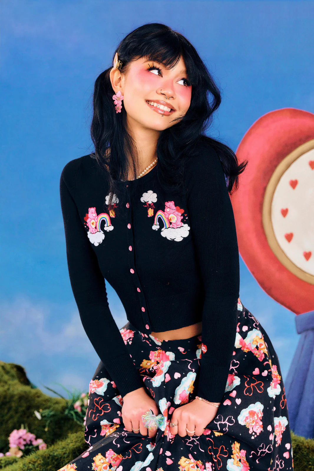 Woman wearing a black cardigan with floral designs and a floral skirt against a colorful background