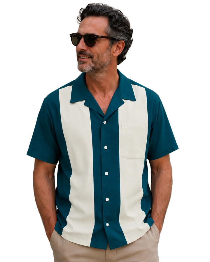 Middle-aged man wearing a teal and cream striped short-sleeve bowling shirt with beige pants and sunglasses, standing casually with hands in pockets against white background