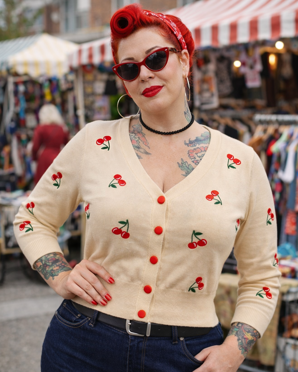 Woman wearing a vintage-style cardigan with cherry patterns at an outdoor market.