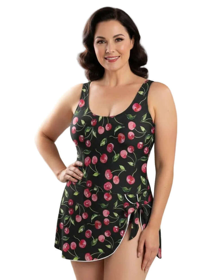 Black Cherries One Piece Skirted Swimsuit modeled by a woman, featuring a cherry print and elegant skirted design.