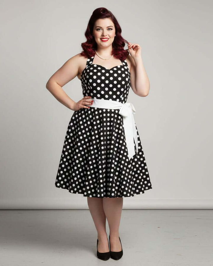 Woman wearing a Black Polkadot Rockabilly Swing Dress with a white belt, showcasing vintage style.