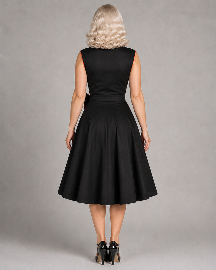 A woman viewed from the back wearing a sleeveless black dress with a fitted waist and full flared skirt, paired with black heels, against a plain gray studio background.