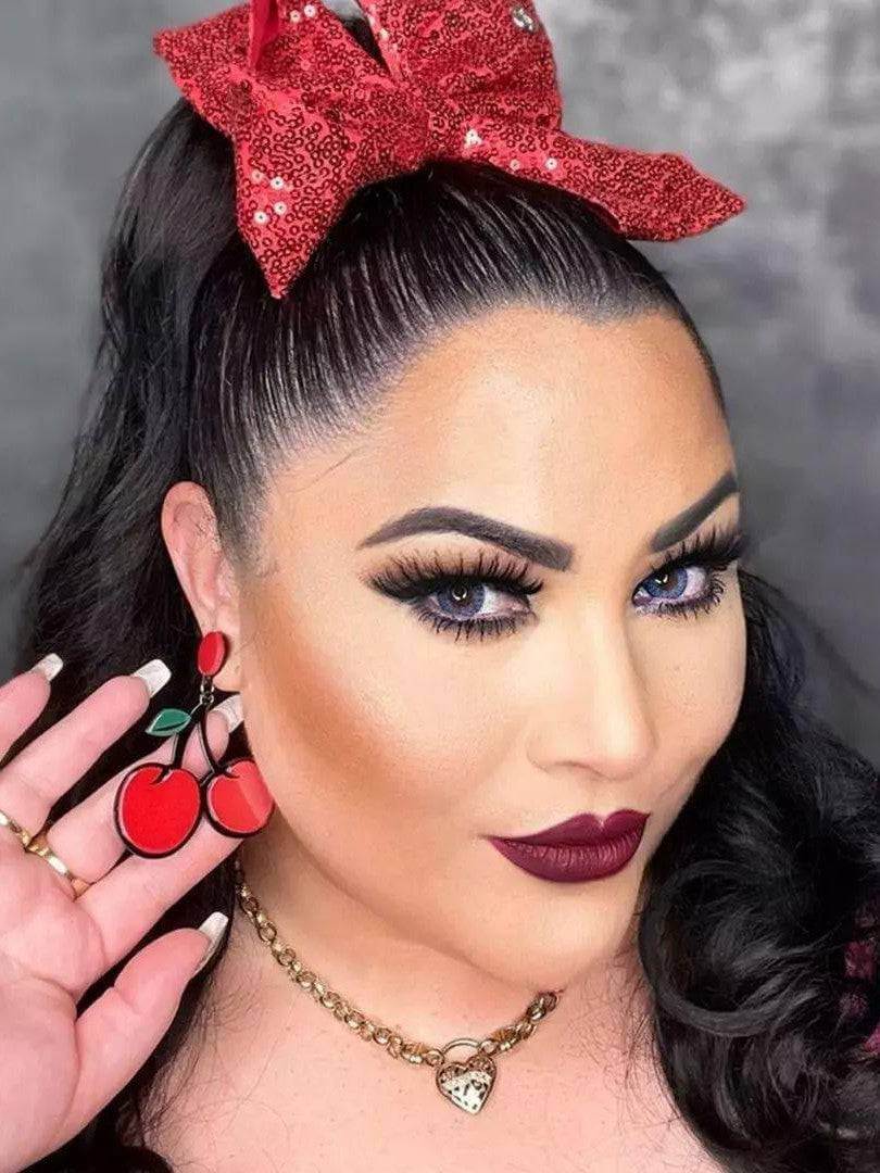 Woman showcasing CHERRIES Acrylic Drop/Dangle Stud Earrings, vibrant red cherries with a stylish bow in her hair.