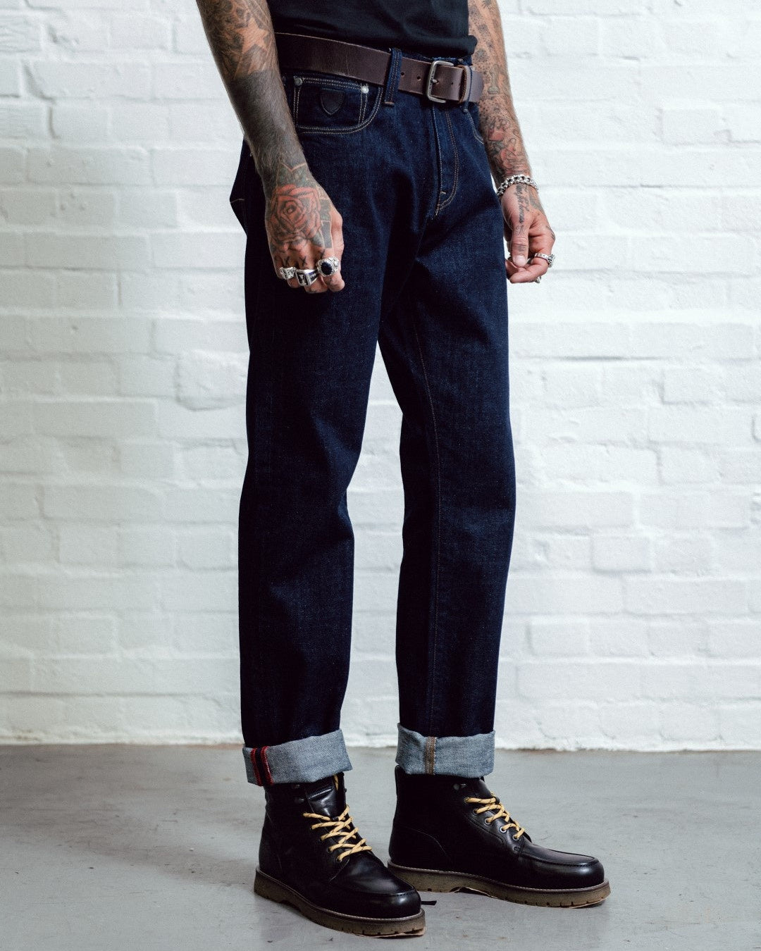 Person wearing dark jeans and black boots against a white brick wall.