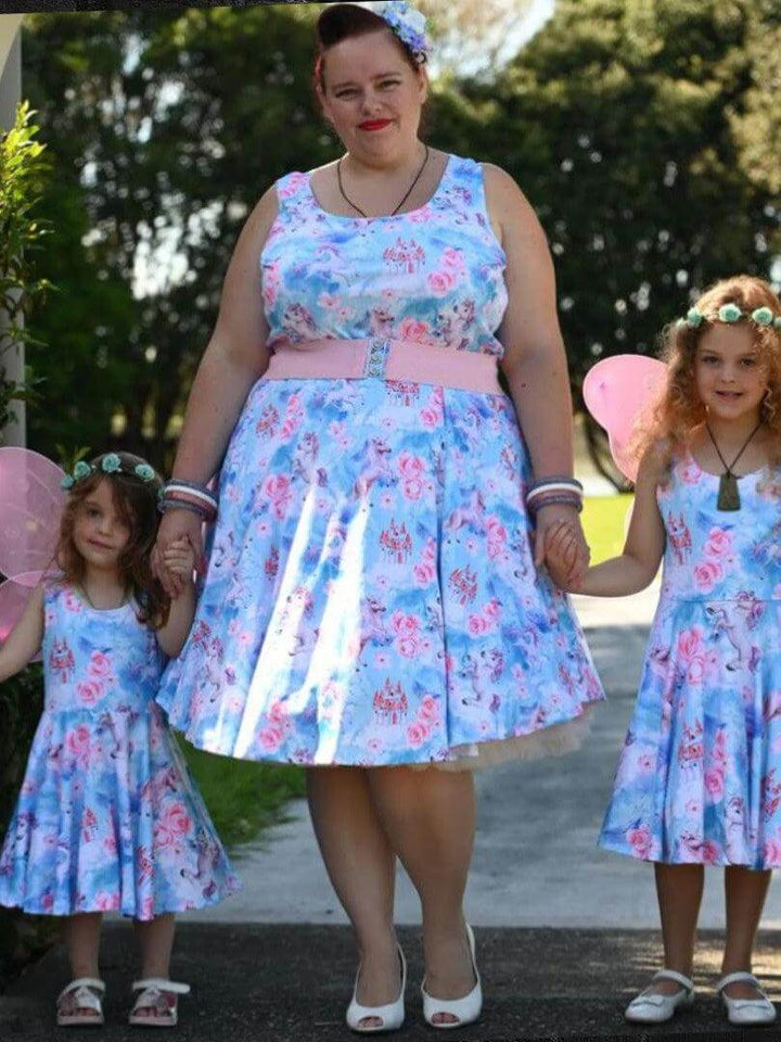 Woman in a floral knee-length skater dress with two girls in matching dresses, holding hands outdoors.