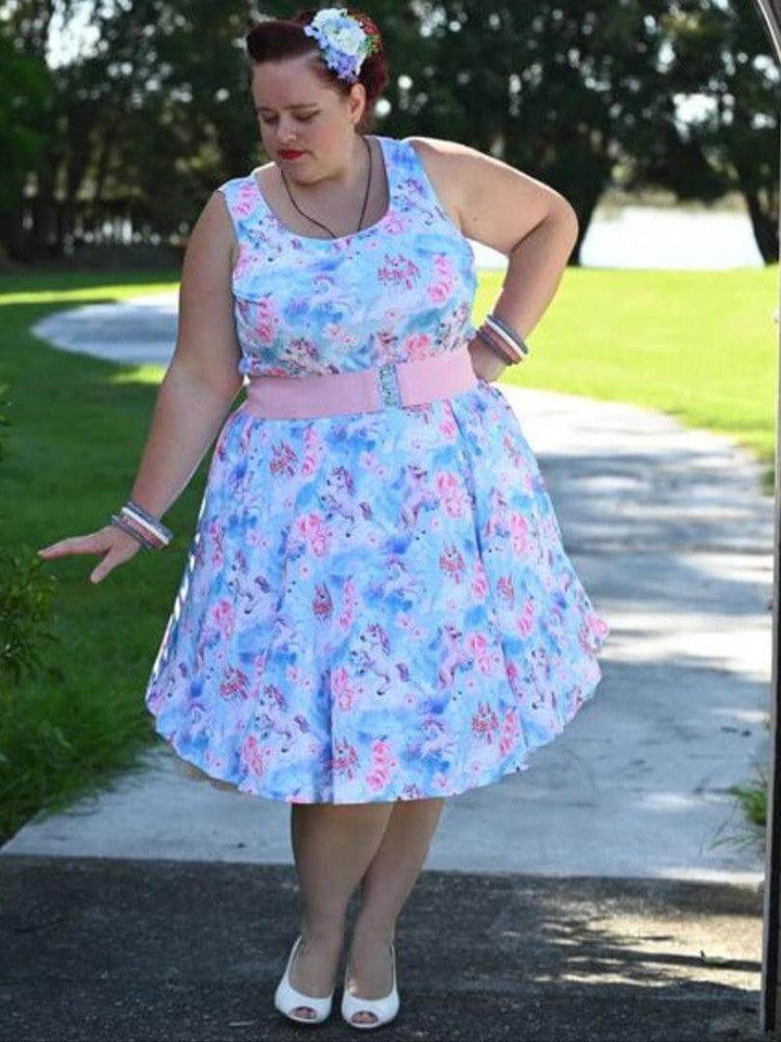 Woman wearing a fantasy unicorn knee-length skater dress with floral print and pink belt, enjoying a sunny day outdoors.