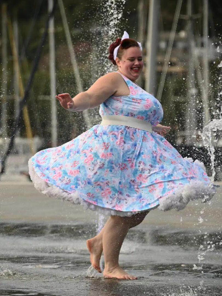 Woman twirling in a knee-length unicorn skater dress in a water fountain, enjoying a playful and vibrant look.
