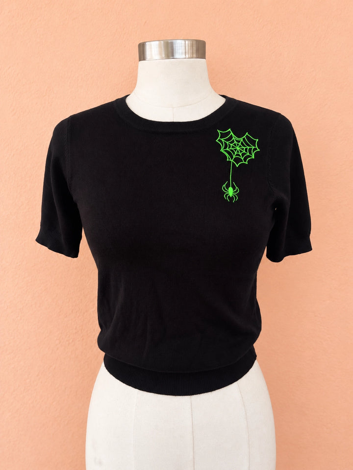 Black knit top with neon-green spiderweb and hanging spider embroidery on mannequin