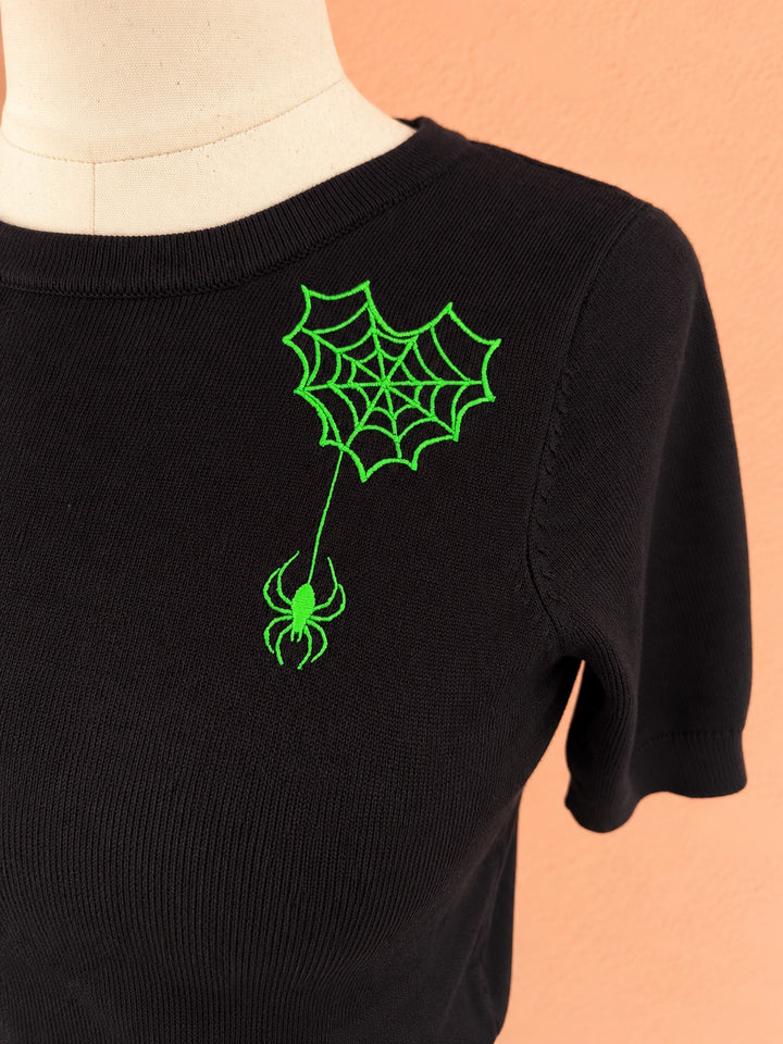 Close-up of neon-green spiderweb and spider embroidery on black knit fabric