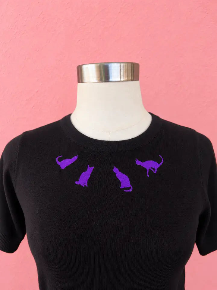 Black knit top with four purple embroidered cat silhouettes around the crew neckline