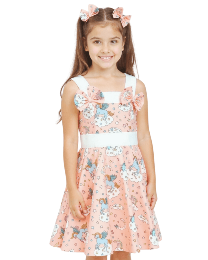 Girl wearing a Peach Unicorns Rockabilly Dress with bows, featuring bright unicorn prints on a playful circle skirt.