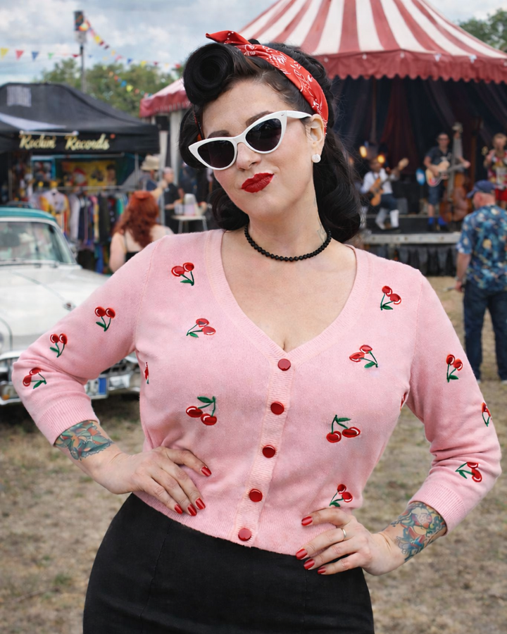 Woman wearing a pink cardigan with cherry designs at a vintage fair.