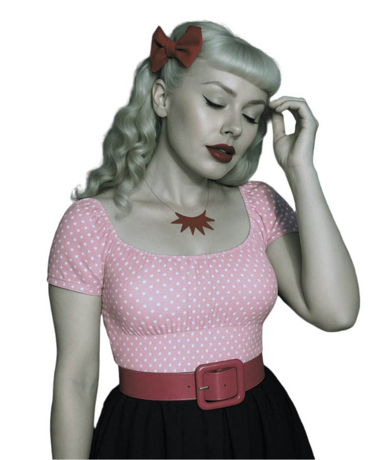 Woman wearing a pink polka dot top with a red belt and a red bow in her hair.