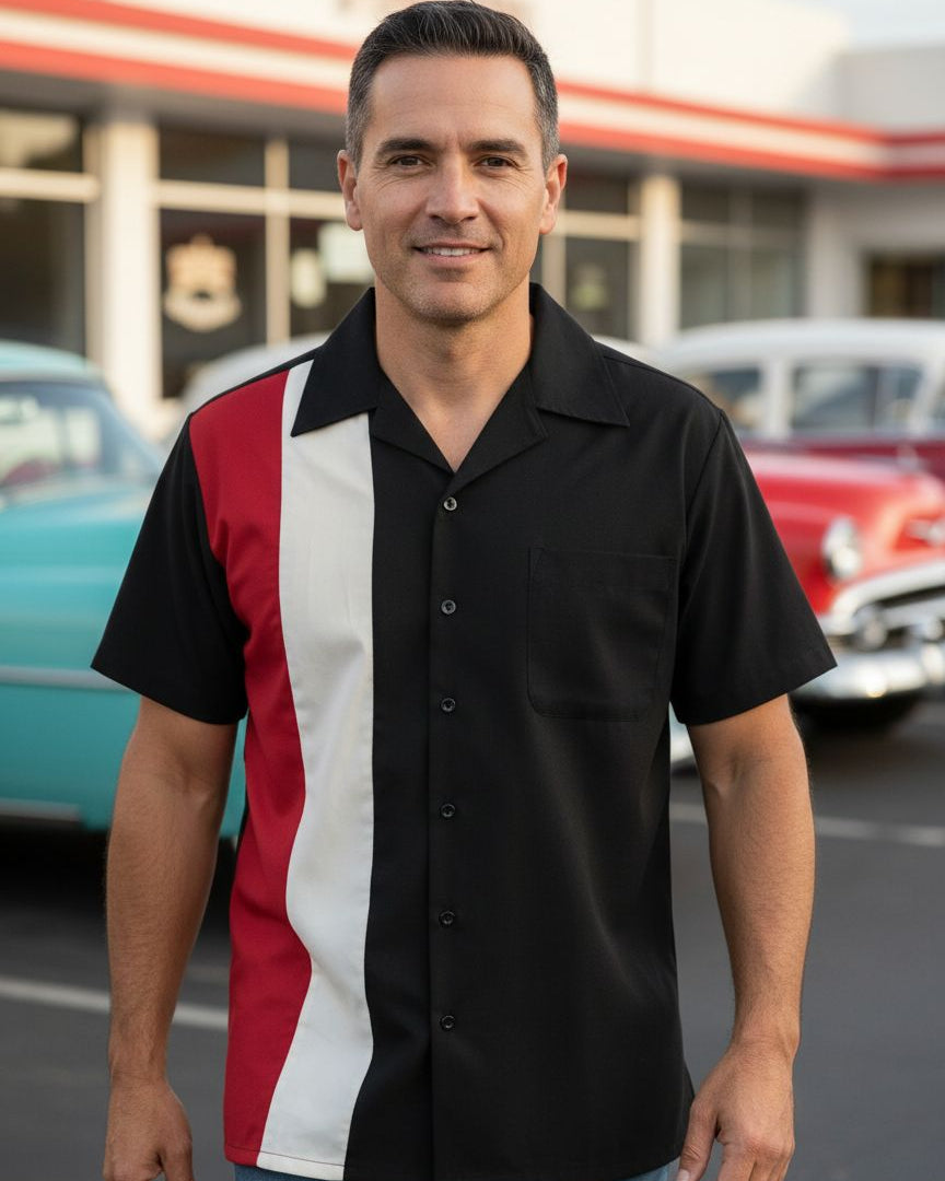 Man wearing a black, red, and white striped shirt standing in front of vintage cars.