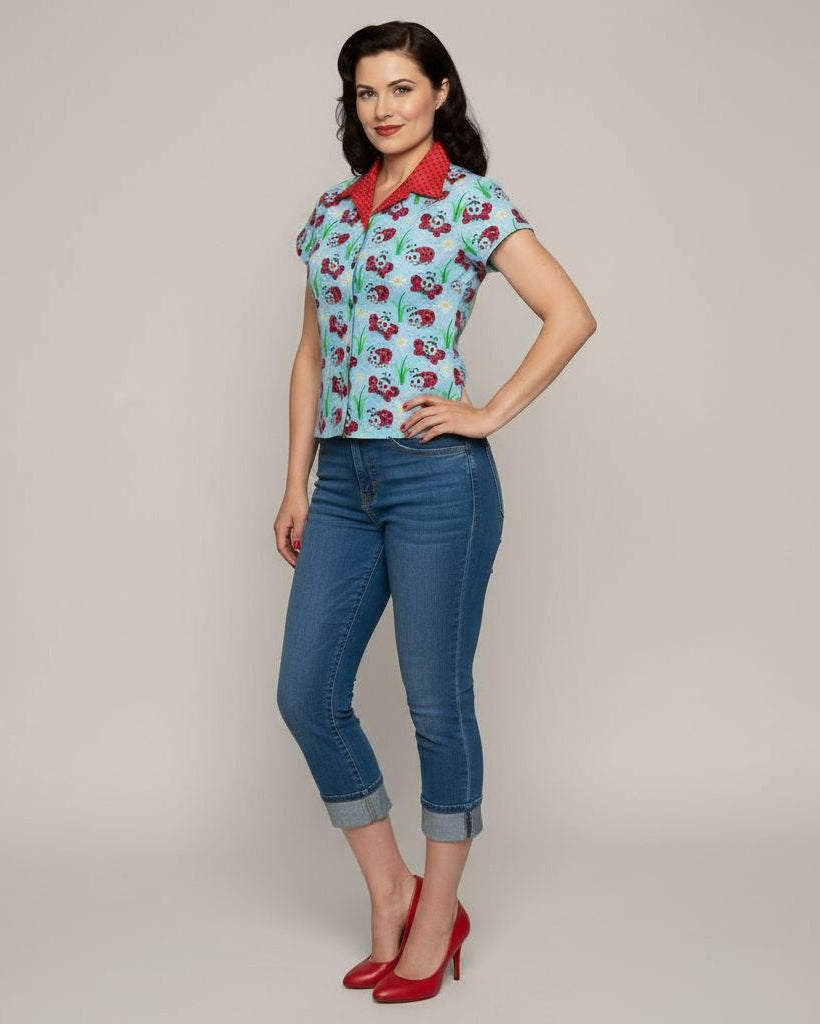 Woman wearing a patterned shirt and blue jeans with red shoes on a plain background