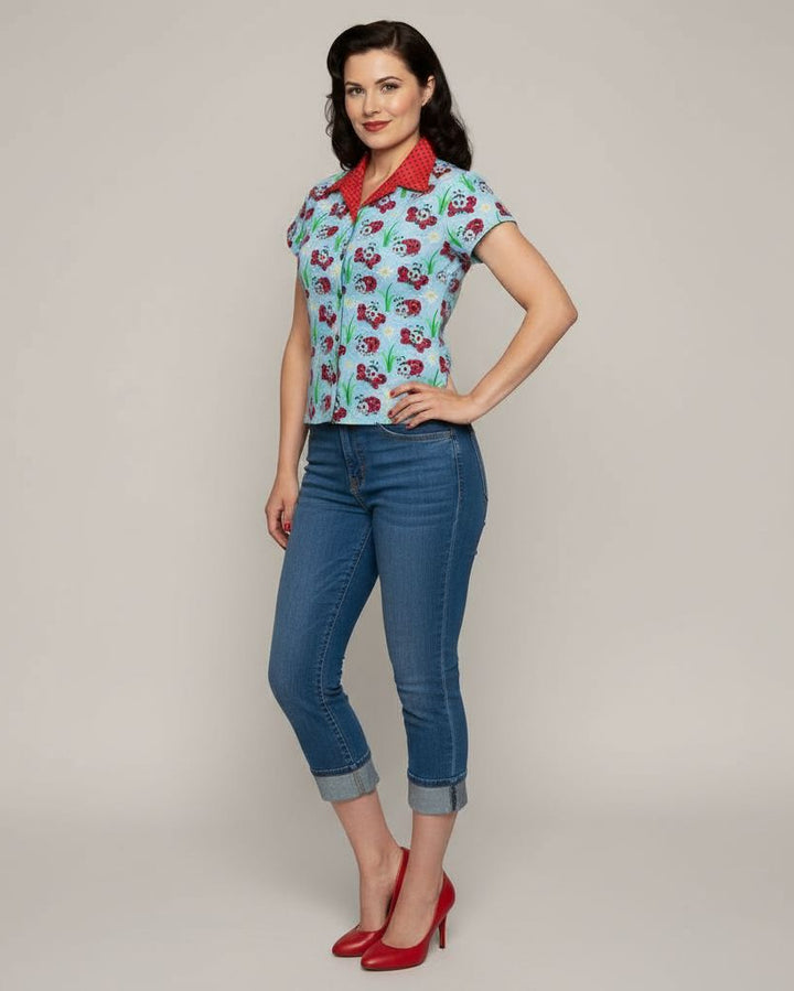 Woman wearing a patterned shirt and blue jeans with red shoes on a plain background
