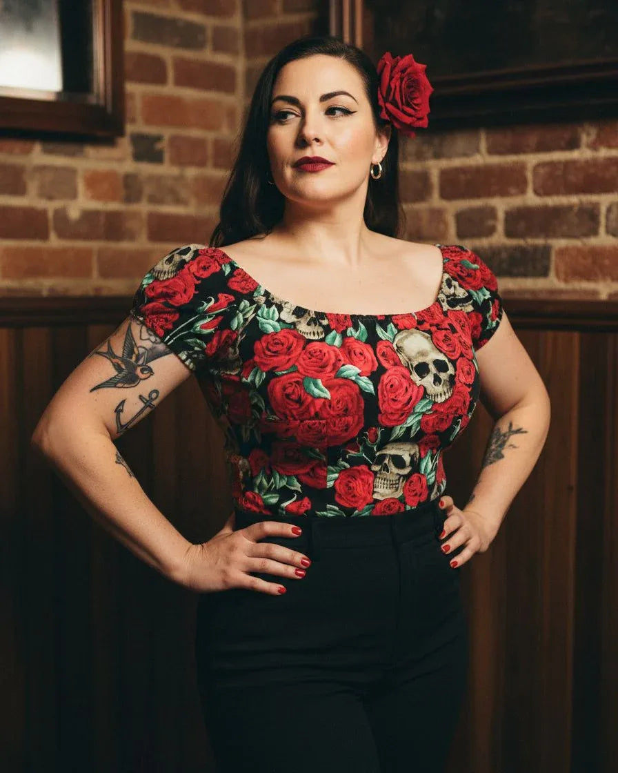 Woman wearing a floral top with red roses and black skulls against a brick wall.