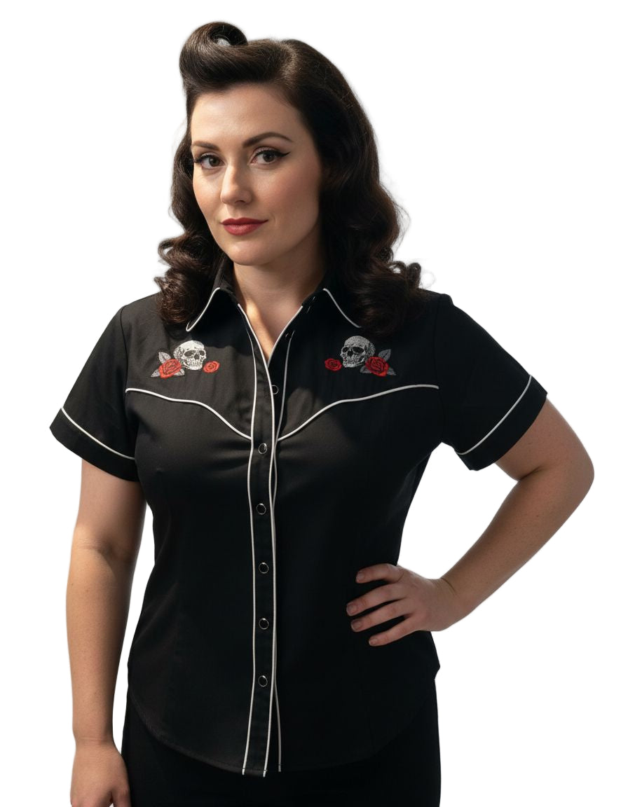 Woman wearing a black shirt with white accents and embroidered skull and roses designs on a plain background