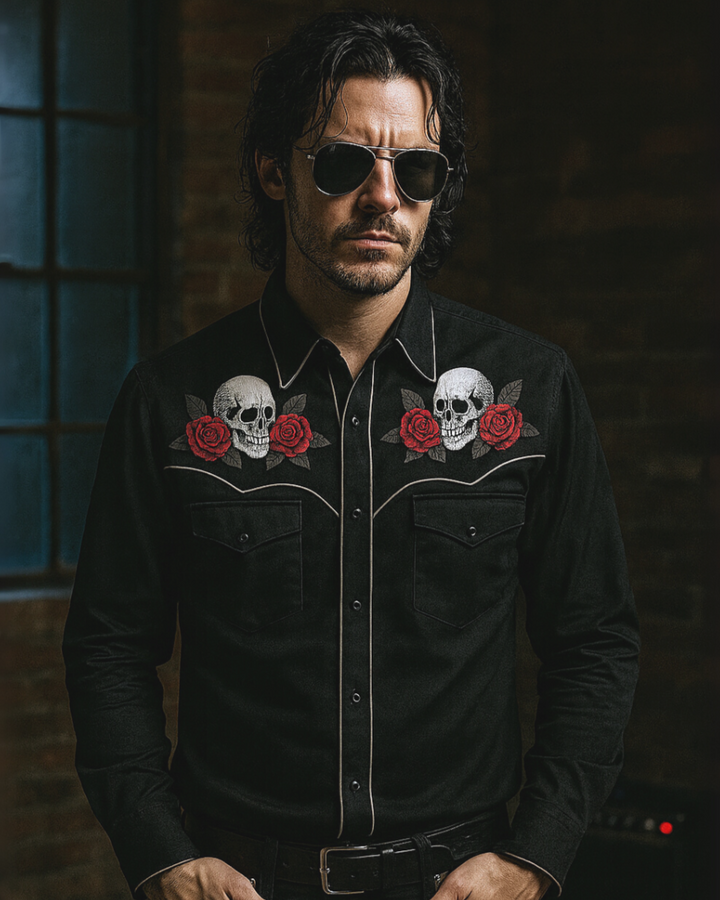 Man wearing a black shirt with skull and rose designs in a dimly lit room.